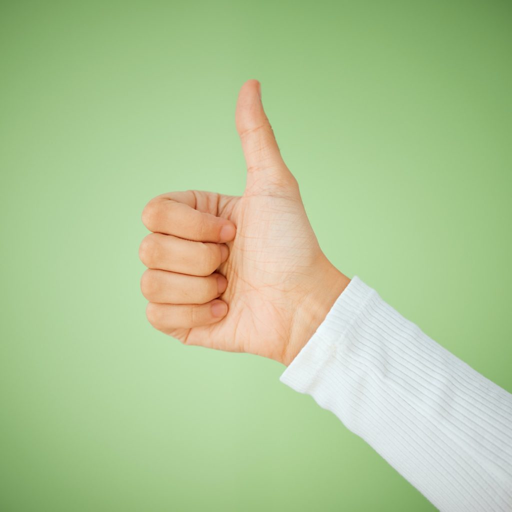 Shot of an unrecognizable woman showing a thumbs up against a green background